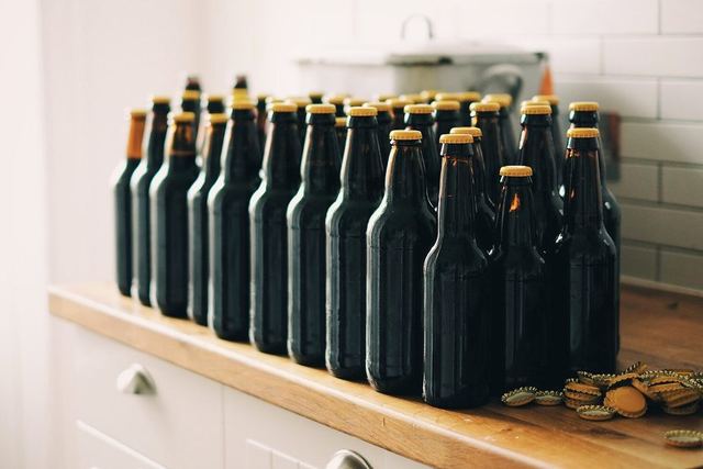Reihe dunkler Bierflaschen mit Kronkorken auf einer Küchenarbeitsplatte