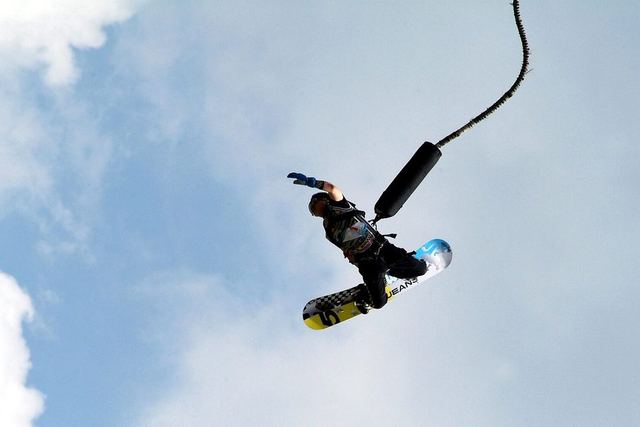Person springt kopfüber an einem Bungee-Seil vor blauem Himmel