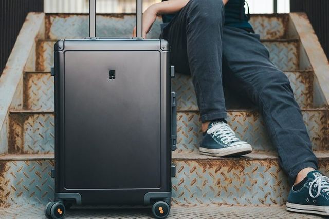 Person sitzt mit schwarzem Hartschalen-Trolley auf einer Treppe